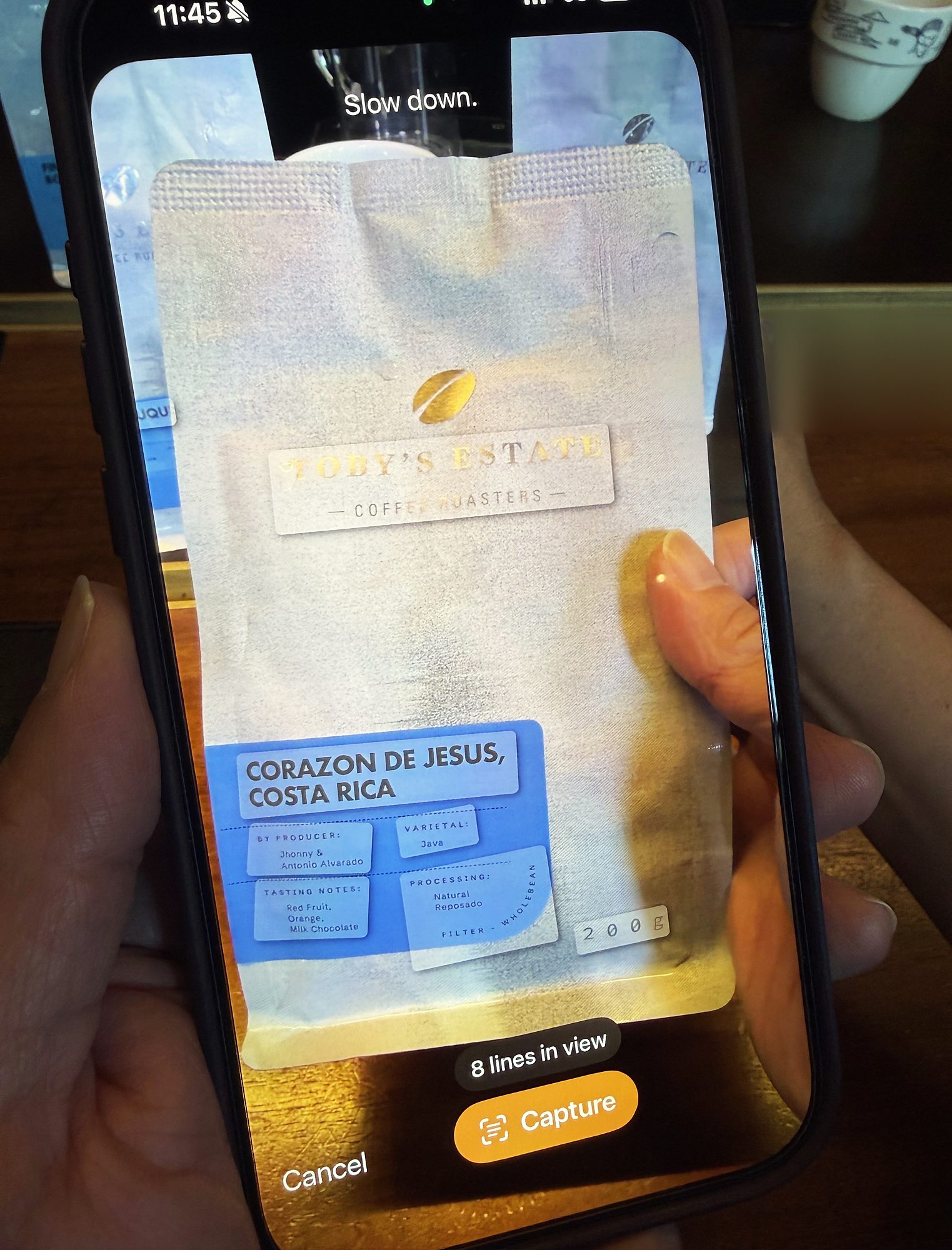 A phone held over a coffee bag, its camera view reading the Corazon de Jesus, Costa Rica label, with the words slow down, eight lines in view, and a Capture button
