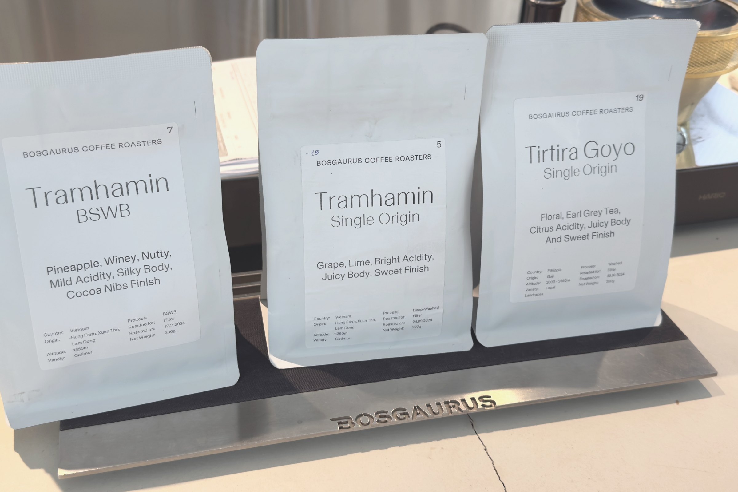 Three bags from Bosgaurus Coffee Roasters, each printing country, origin, altitude, variety, process, roast date and weight; two are from the same Vietnamese farm and differ only in process